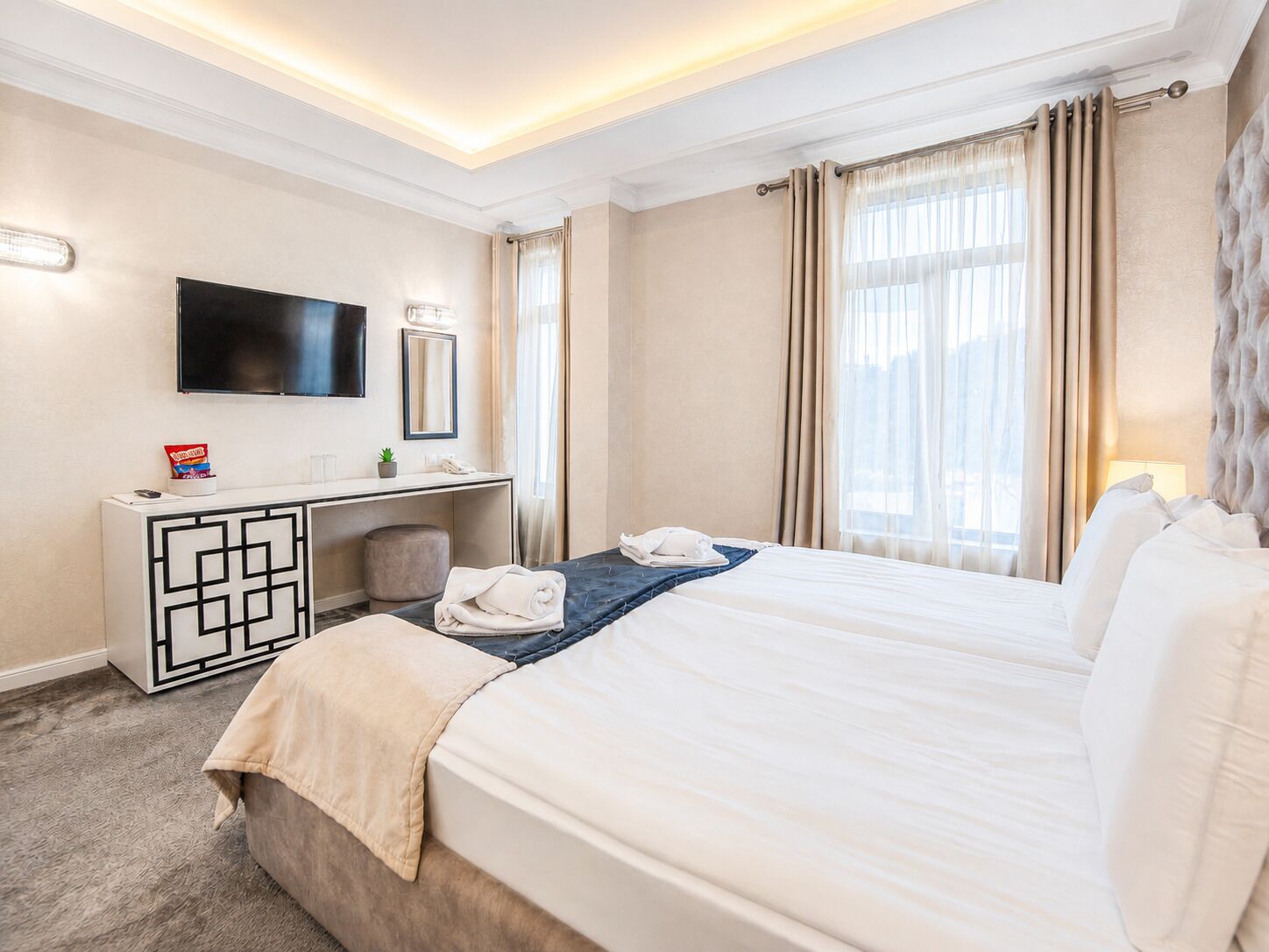 Camera d'albergo con un letto, una scrivania con TV a schermo piatto, uno specchio e una finestra con tende.