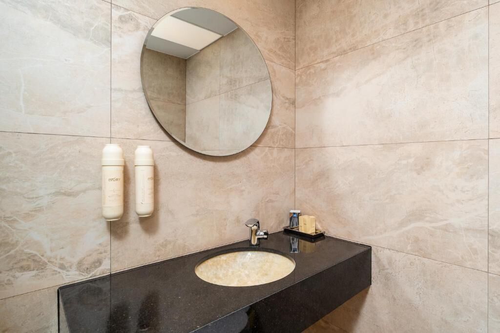 A bathroom with a round mirror, a sink, and two bottles of lotion on the wall.