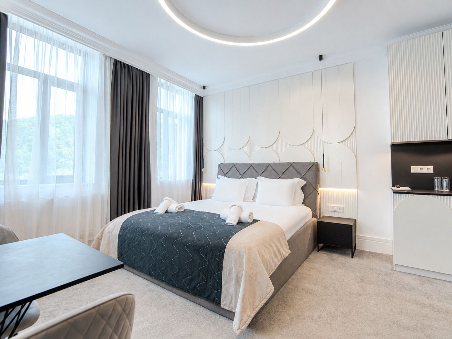 Une chambre d’hôtel moderne, équipée d’un lit, d’une table de chevet et offrant une vue sur l’extérieur.