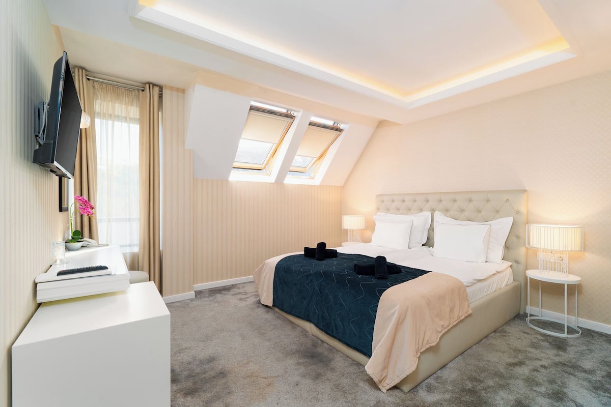 A hotel room with a bed, a TV, a desk, and a window with curtains.