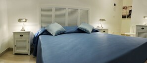 Un dormitorio con una cama, dos mesitas de noche y cabecera con listones horizontales.