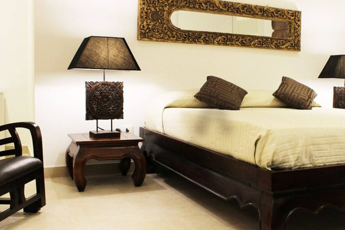 Quarto bem arrumado com uma cama grande, duas mesas de cabeceira com luminárias, uma cadeira e um espelho na parede.