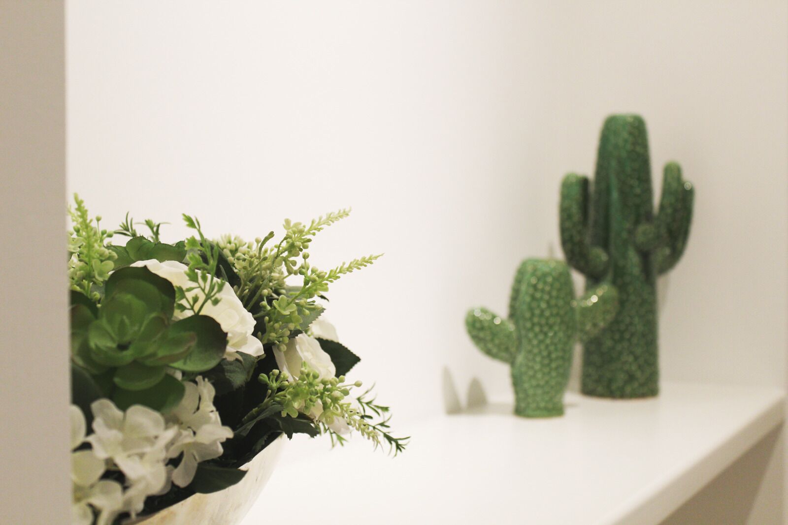 A white shelf with a potted plant and two cactus sculptures.