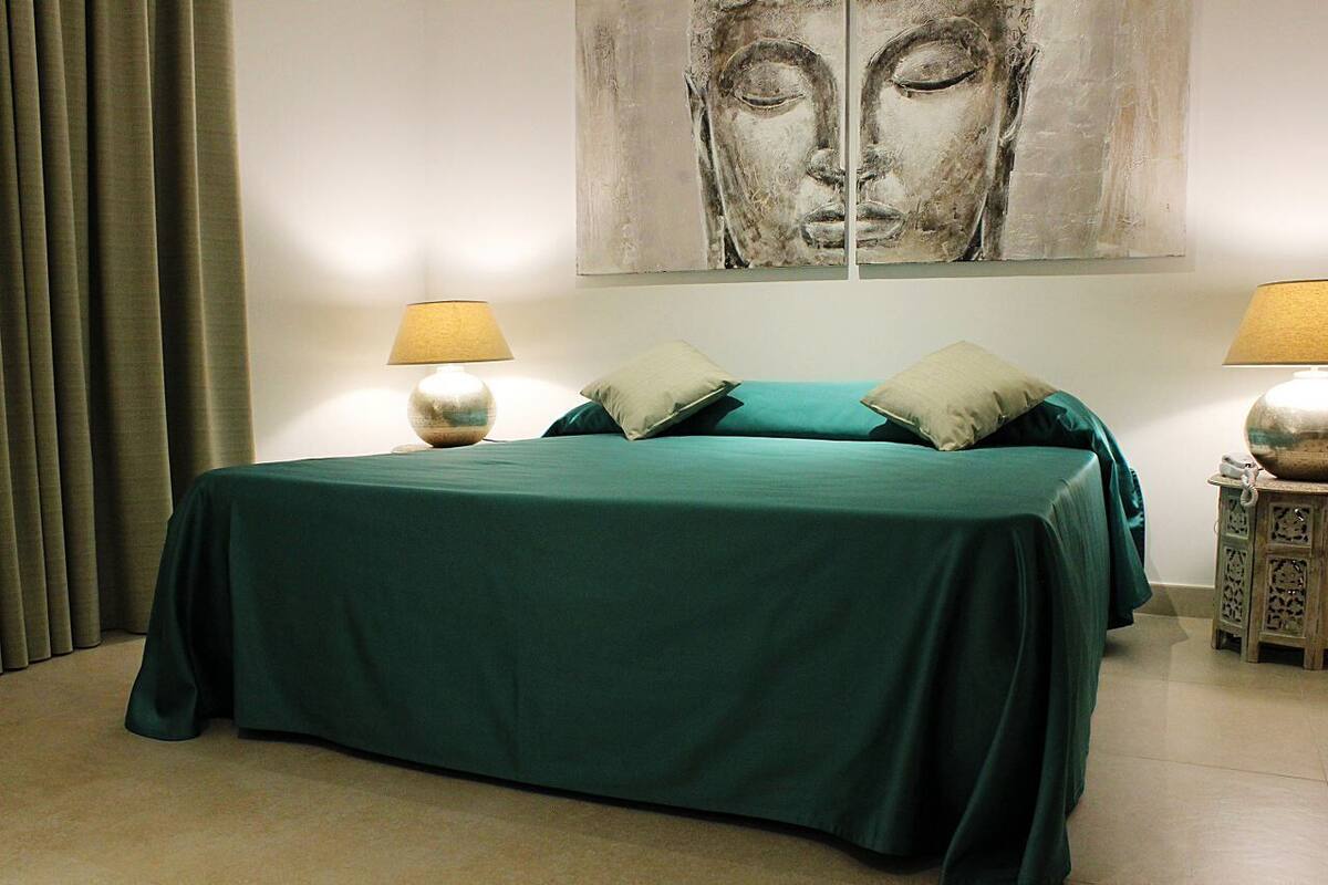 Uma cama com colcha verde, duas almofadas e duas luminárias de cabeceira.