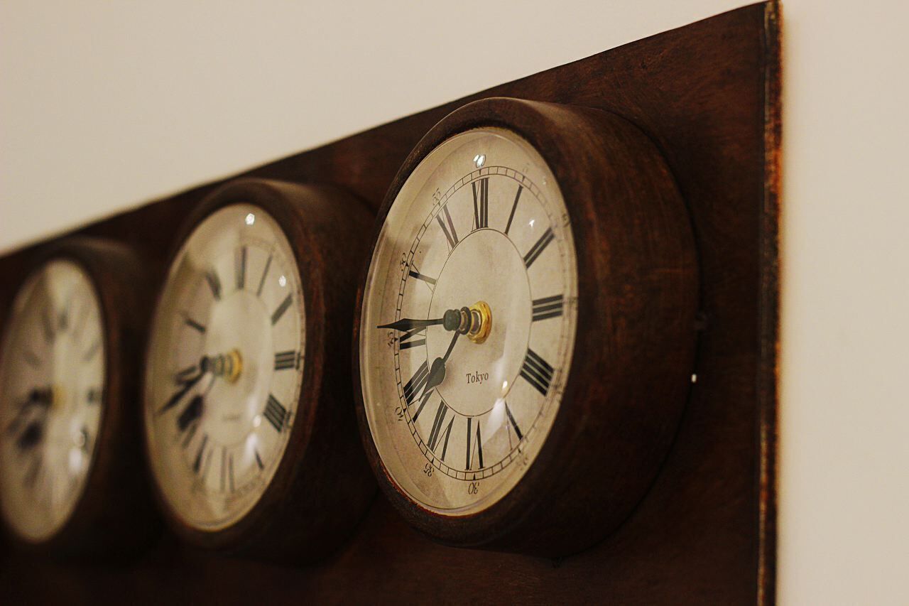 Una hilera de relojes de pared con números romanos, cada uno marcando una hora distinta.
