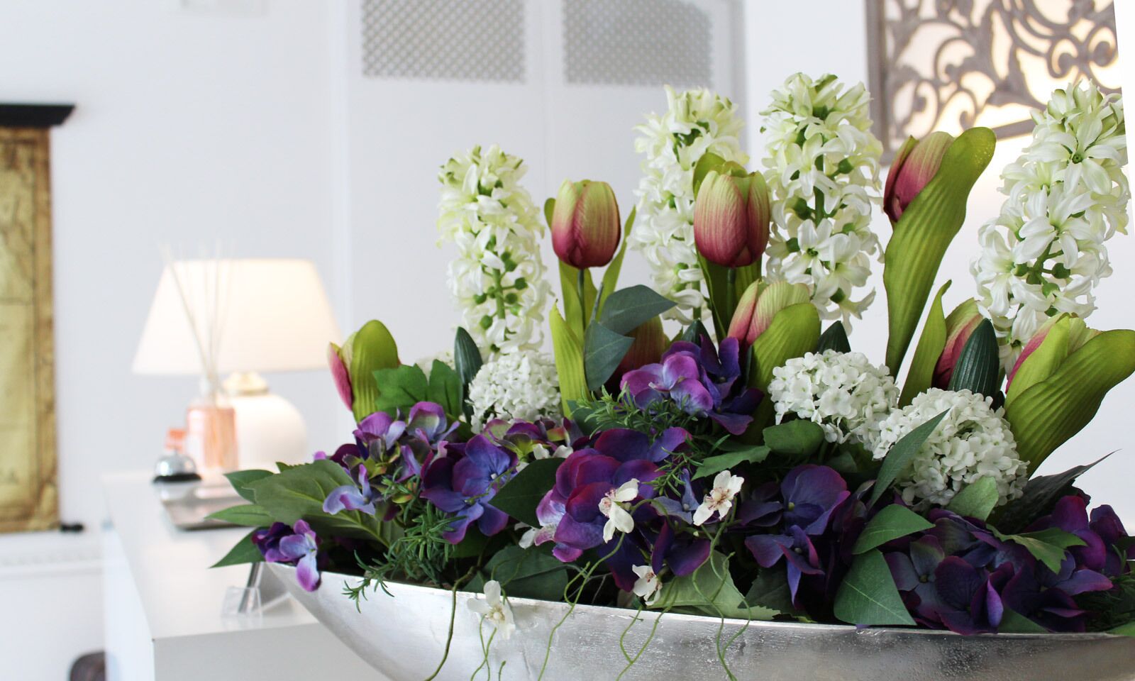 A floral arrangement in a metal vase on a white surface.