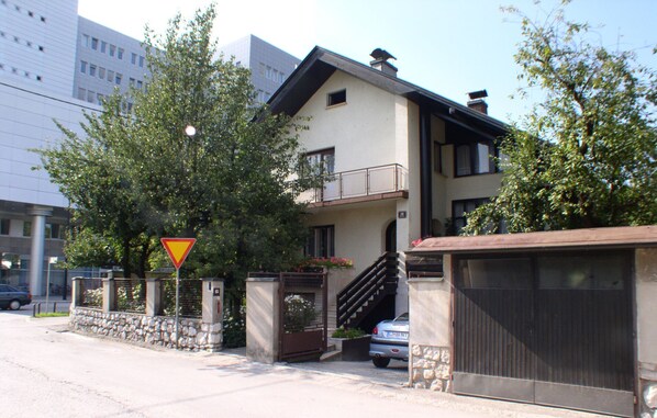 A two-story building with a balcony on the second floor, a stone wall, and a car parked in front.