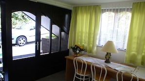 Ein Zimmer mit Schreibtisch, zwei Stühlen, einer Lampe und einem Fenster mit gelben Vorhängen.