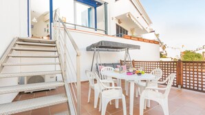Un patio con una mesa redonda y sillas blancas, una escalera y un ventanal con marco azul.