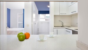Una cocina moderna con armarios blancos, un lavamanos y una ventana. Hay dos manzanas y una naranja en la encimera.