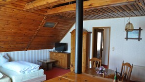 Una habitación acogedora con techo de madera, una cama, una mesa de madera y un televisor sobre un mueble.