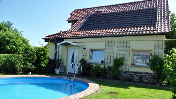 Una casa con piscina, techo de tejas y un borde de ladrillo alrededor de la piscina.