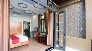 A bedroom with a bed, a desk, and a chair. There is a window with curtains, a mirror, and a wall with a textured pattern. - Tan Doan An Bang center beach villas (Tp. Hội An)