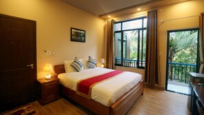 A bedroom with a large bed, a nightstand with a lamp, a door, and a window with curtains. - Tan Doan An Bang center beach villas (Tp. Hội An)