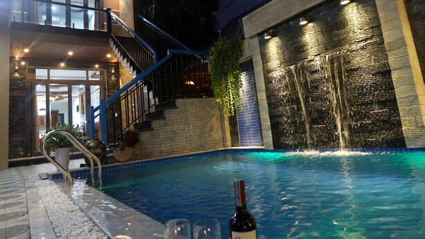 A swimming pool with a waterfall feature, a staircase leading to a balcony, and two wine glasses and a bottle on the poolside. - Tan Doan An Bang center beach villas (Tp. Hội An)