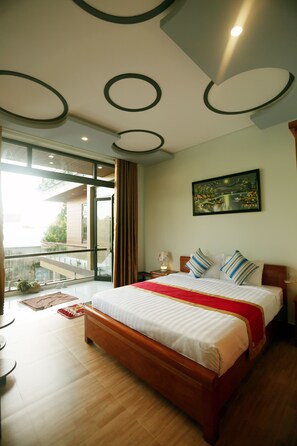 A modern hotel room with a large bed, a balcony with a view, and a painting on the wall.