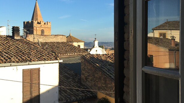 Uitzicht vanuit een raam op een stad met een opvallende kerktoren en pannendaken.