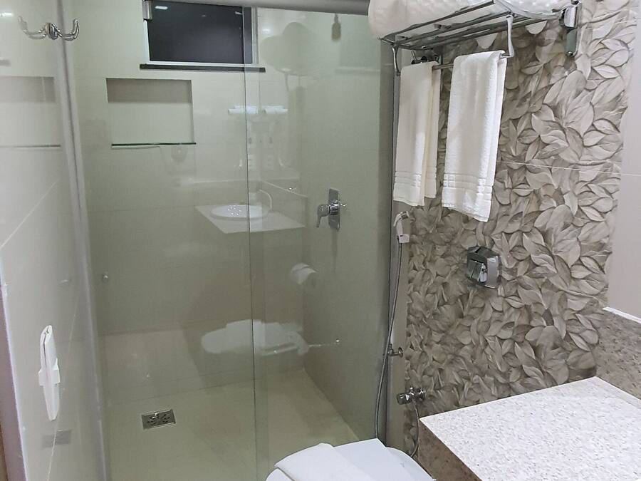 Un baño moderno con ducha envuelta en cristal, inodoro blanco, lavabo y toallero con toallas.