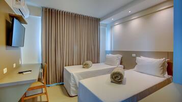 A hotel room with two beds, a desk, a chair, and a TV.