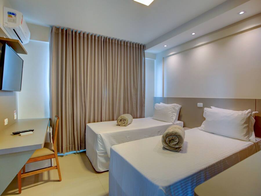 A hotel room with two beds, a desk, a chair, and a TV.