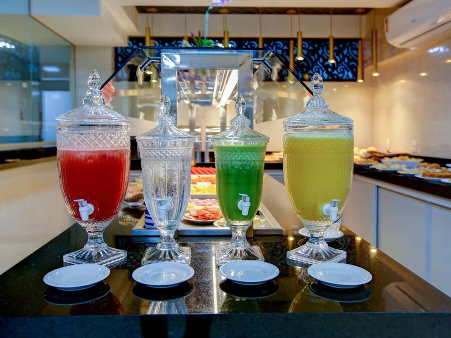 Un buffet avec quatre distributeurs de boissons présentés dans des récipients en verre transparent, chacun étant muni d’un robinet et d’un bec verseur.
