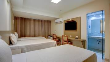 Habitación de hotel con dos camas, un escritorio, una silla, un televisor, un equipo de aire acondicionado y un baño con separador de vidrio.