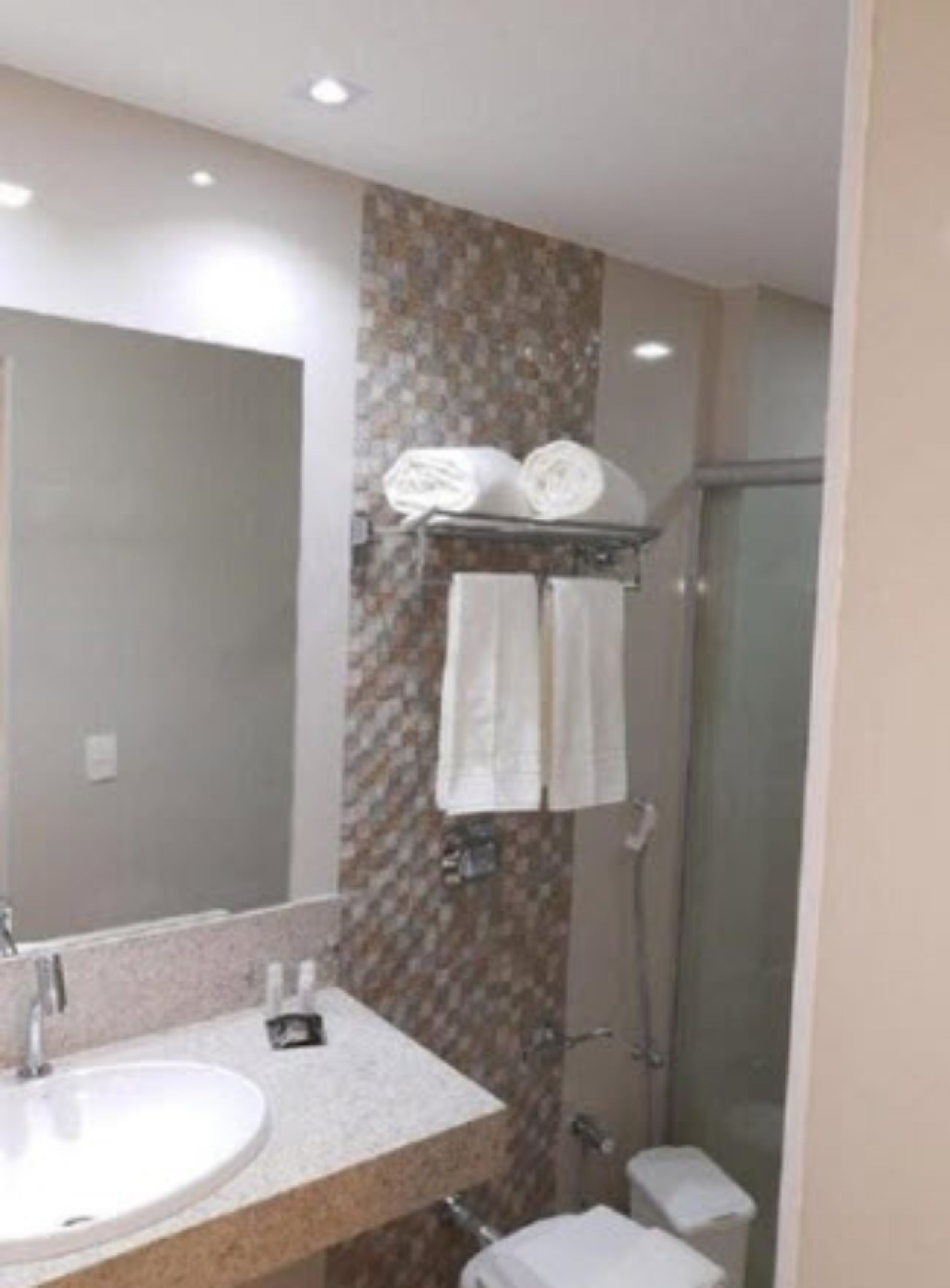 A bathroom with a sink, mirror, shower, and towel rack.