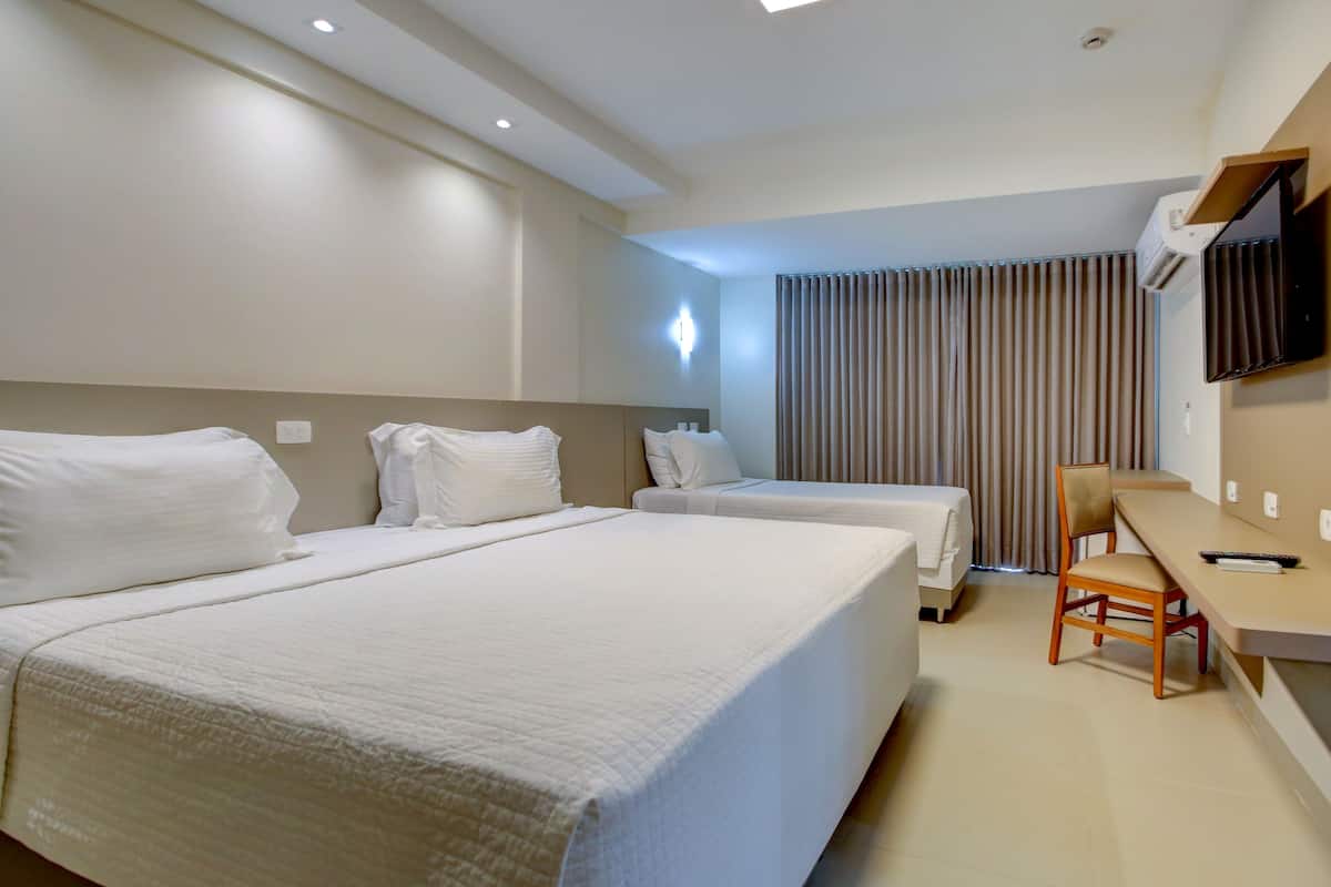 A hotel room with two beds, a desk, a chair, a TV, and a window with curtains.