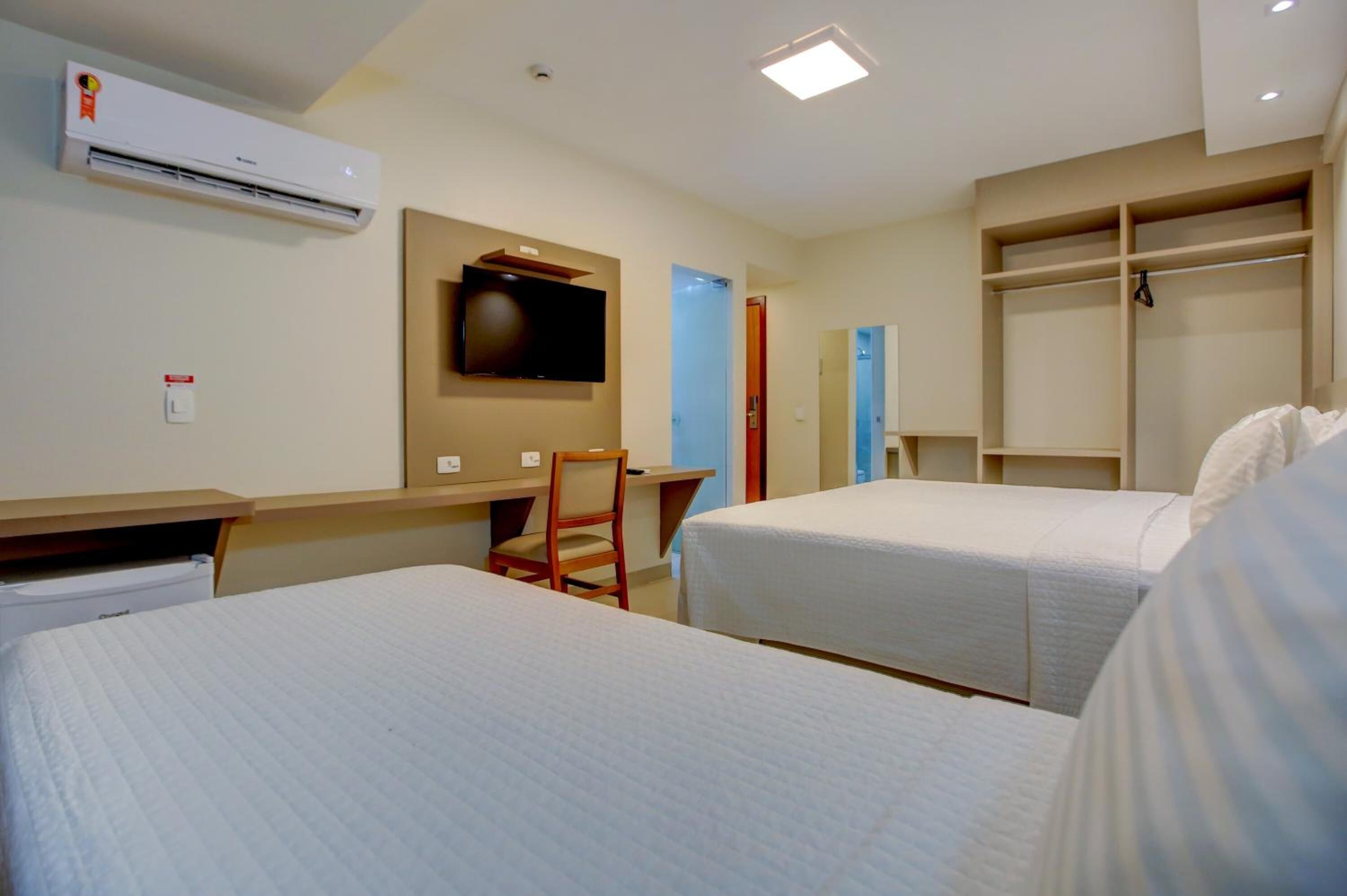 A hotel room with two beds, a desk, a chair, a TV, and a wardrobe.