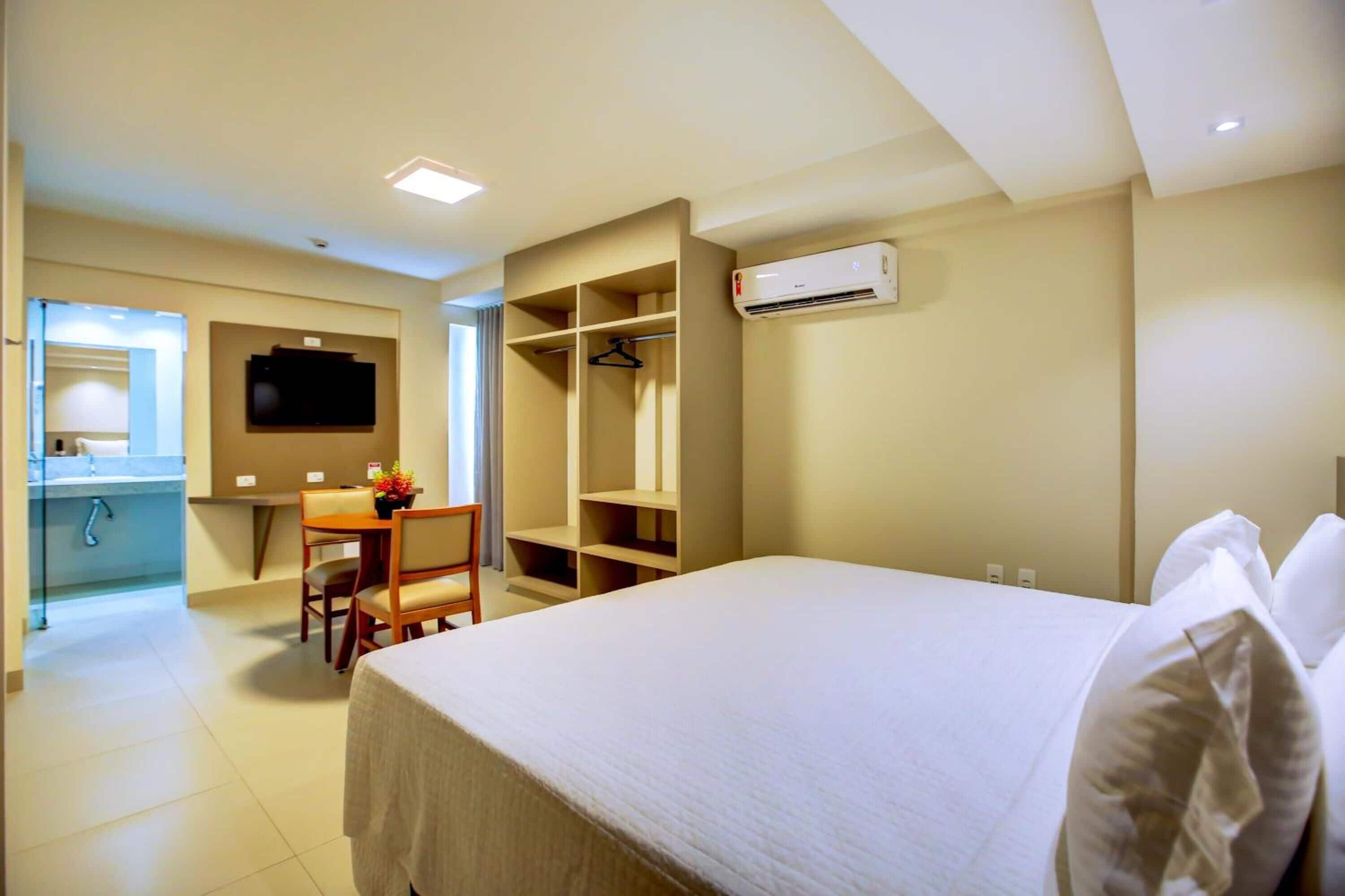 Habitación de hotel con cama, escritorio, silla, armario y equipo de aire acondicionado.