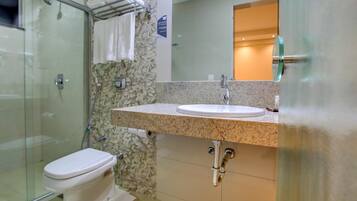 A modern bathroom with a glass shower enclosure, a white toilet, a granite countertop sink, and a mirror above the sink.