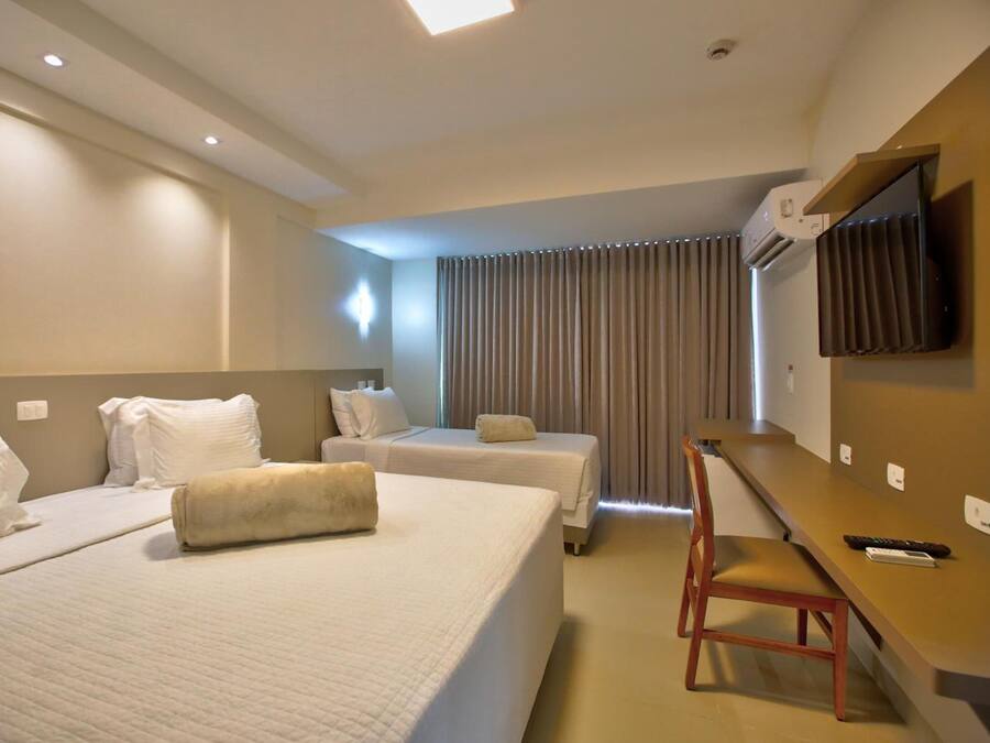 A hotel room with two beds, a desk, a chair, a TV mounted on the wall, and a window with curtains.