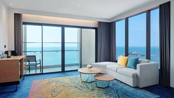A modern hotel room with a large balcony, a sofa, a coffee table, and a desk.