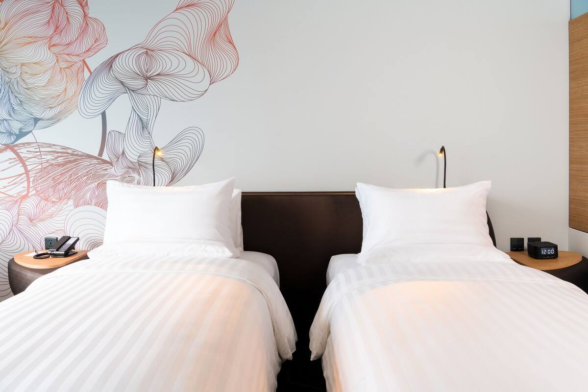 Ein Hotelzimmer mit zwei Betten, einem Wandbild, einem Nachttisch mit Telefon und einem Beistelltisch mit Uhr.