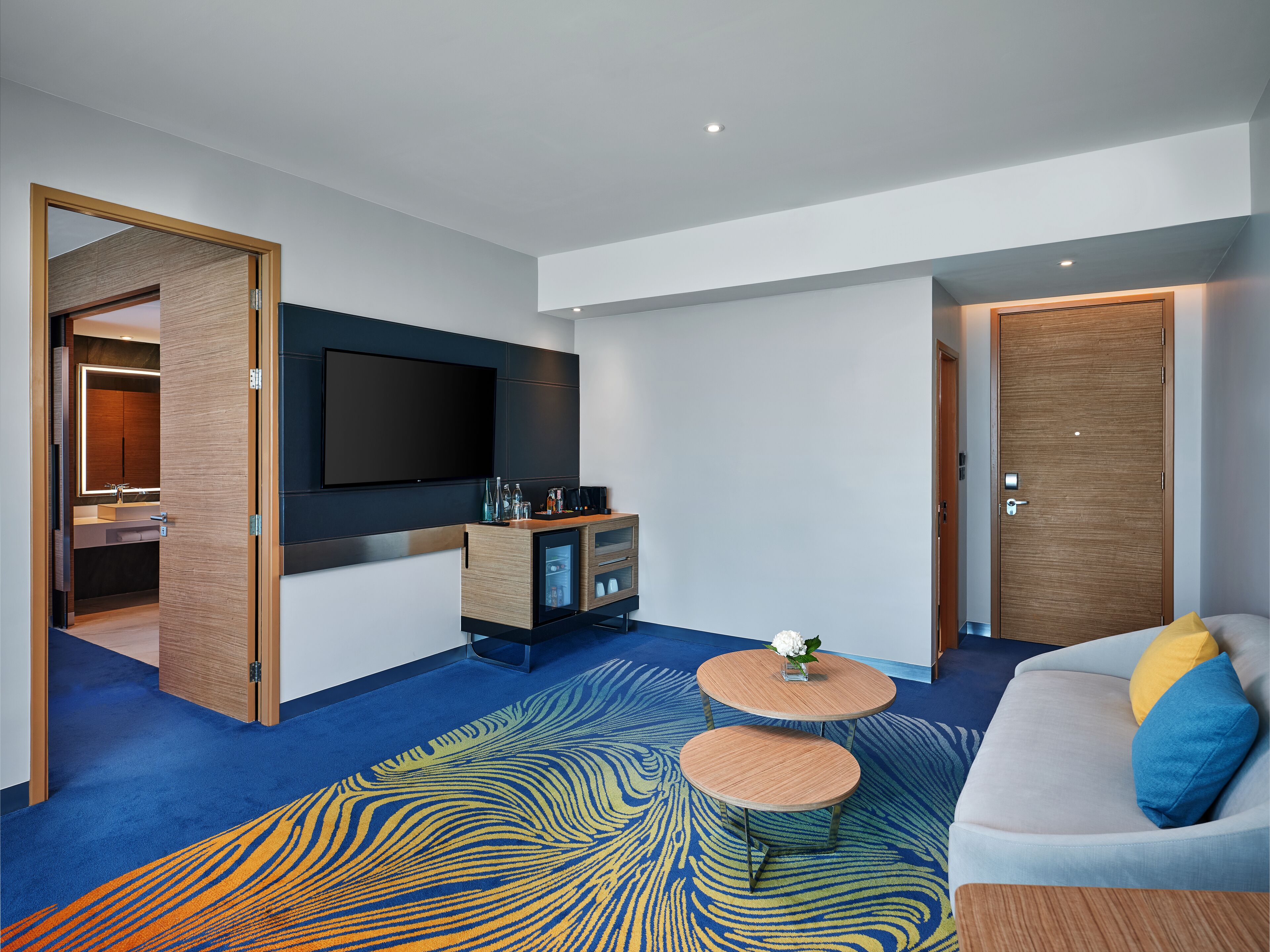 A modern living room with a flat-screen TV, a sofa, two coffee tables, and a patterned carpet.