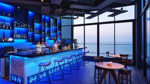 Eine Bar mit Meerblick, die modernes Design, blaues Licht und eine Auswahl an Flaschen zeigt.
