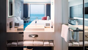 Ein modernes Hotelzimmer mit großem Fenster, einem Bett, einem Badezimmer mit Waschbecken und Spiegel sowie einem Fernseher.