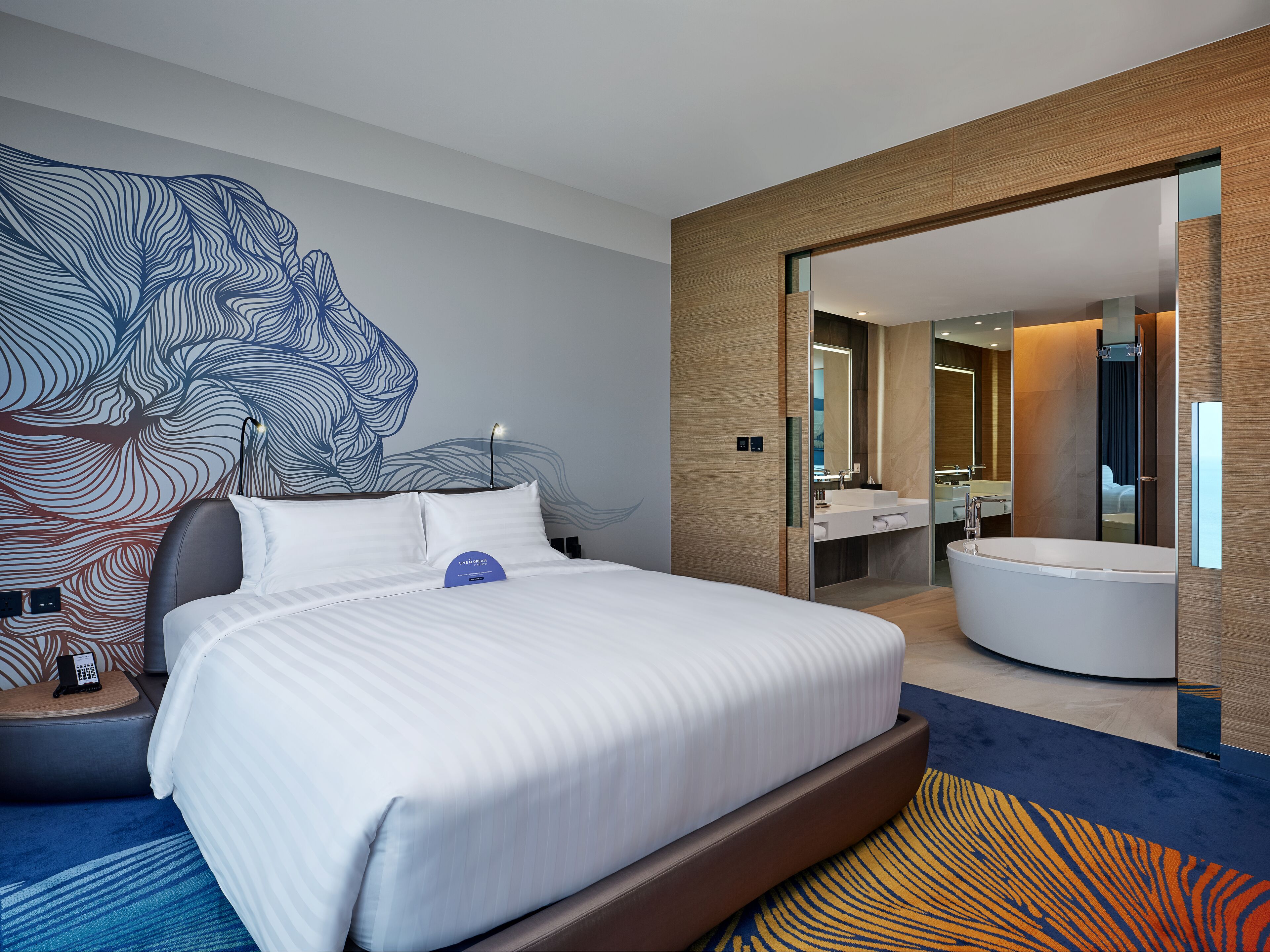 Una habitación de hotel moderna con una cama grande, un baño con bañera y un diseño de arte mural original.