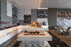 Un restaurante moderno con barra de mármol, diferentes estaciones de comida y una zona de estar con sillas y mesas.