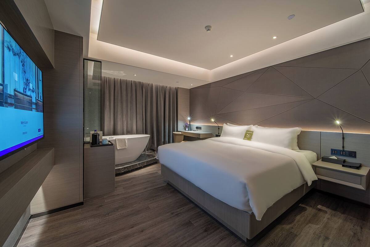 A modern hotel room with a large bed, a TV, a bathroom, and a desk.
