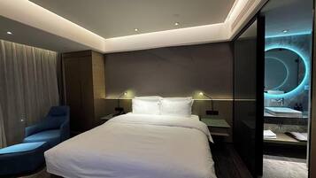 A modern hotel room with a large bed, a desk, a chair, and a bathroom with a circular mirror.