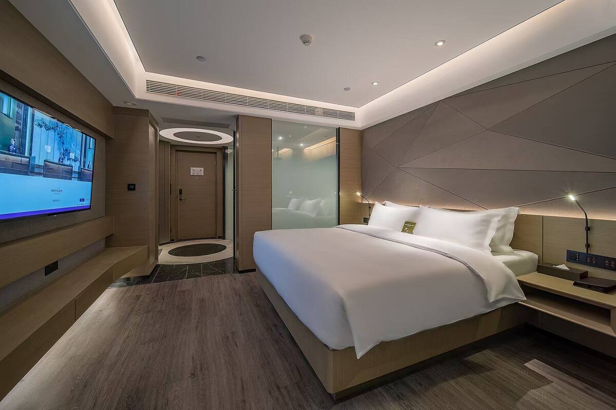 A modern hotel room with a large bed, a TV mounted on the wall, and a sleek design.