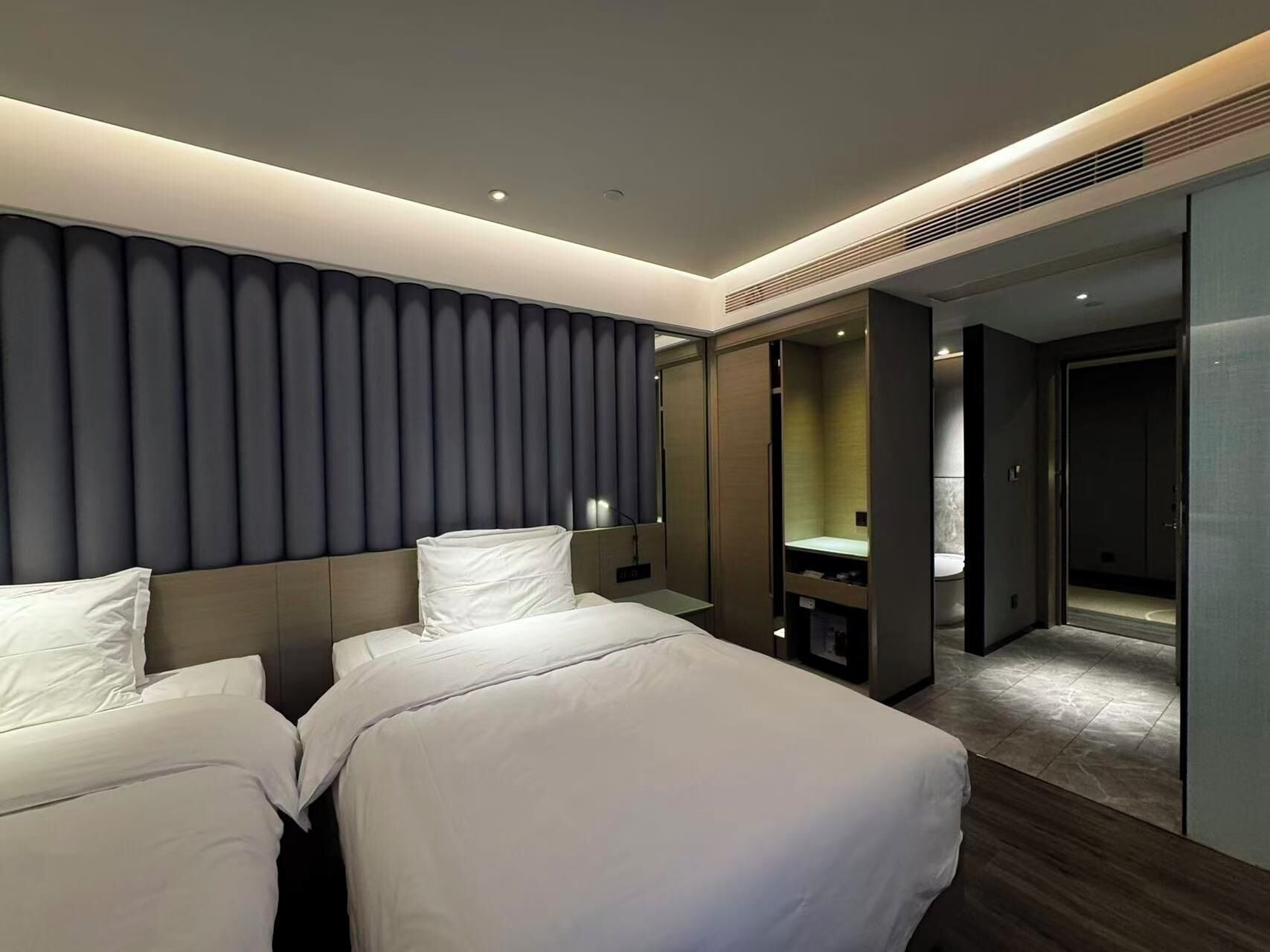 A modern hotel room with two beds, a large mirror, and a walk-in closet.