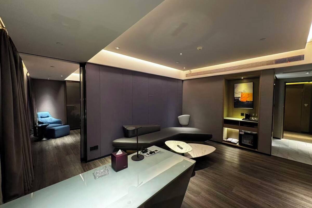 A modern hotel room with a seating area, a desk, and a small kitchenette.