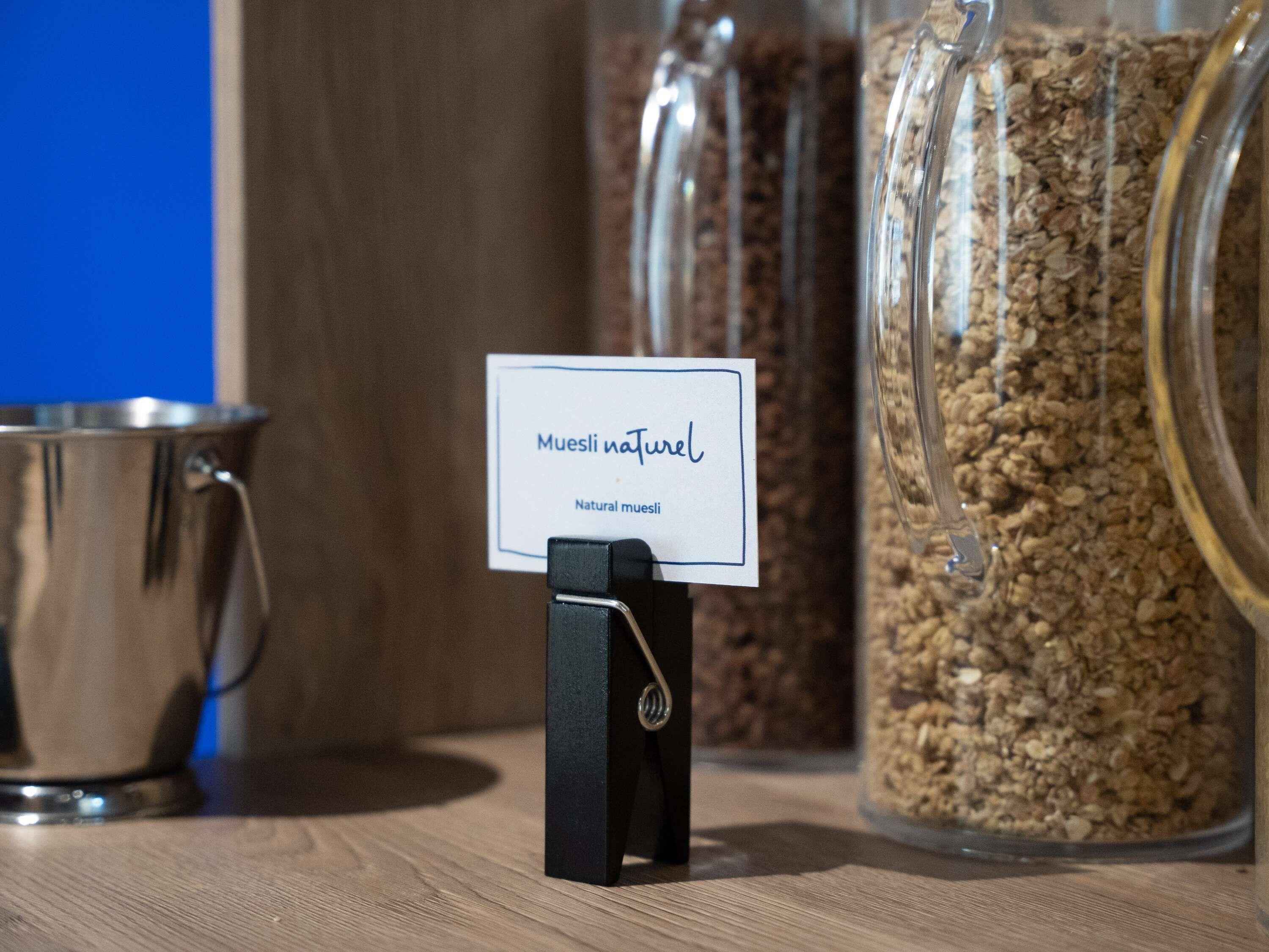 A sign with 'Muesli natural' text, a metal container, and a glass jar filled with granola.