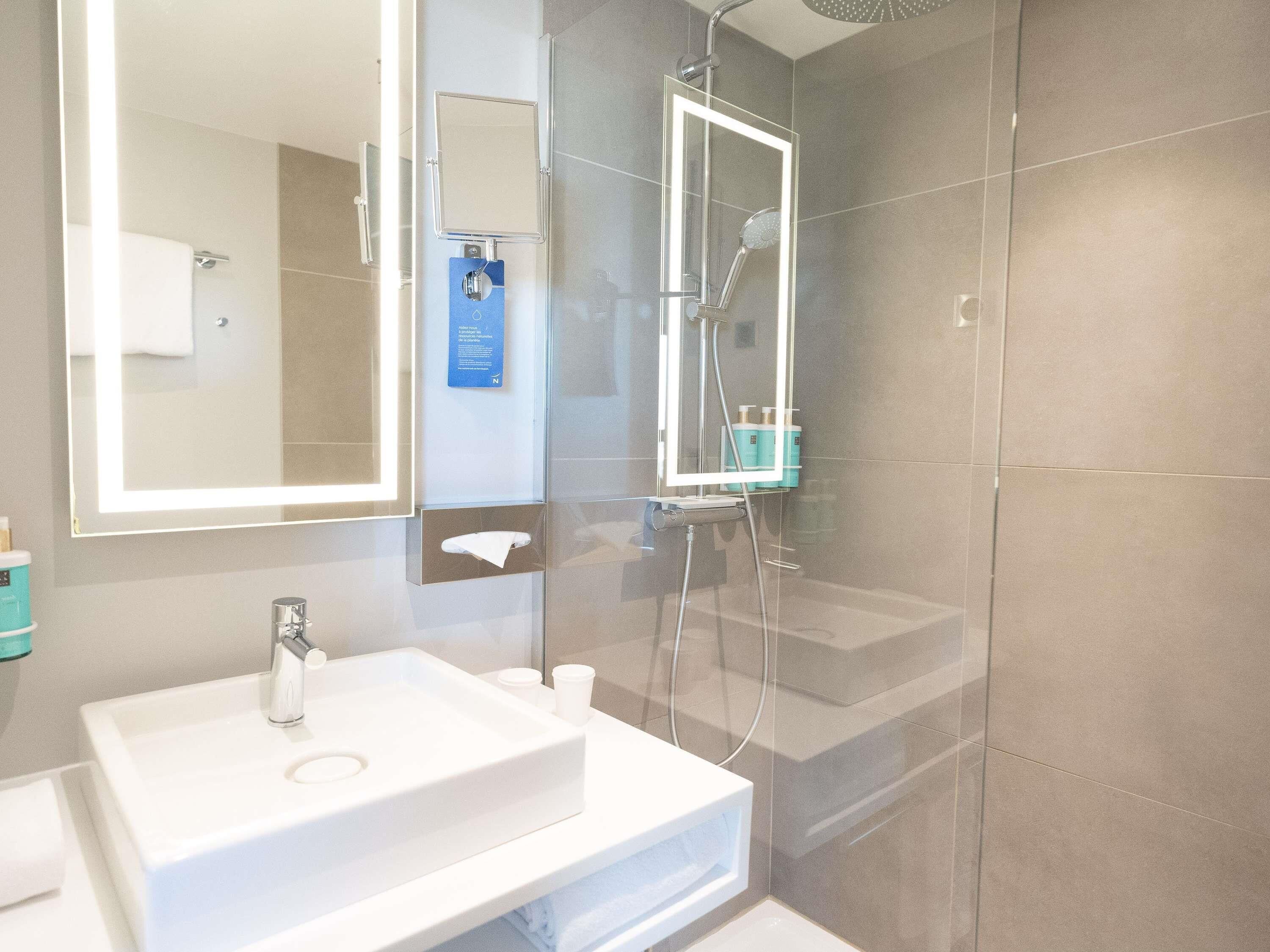 Un baño moderno con un espejo grande, un lavamanos y un box de ducha.