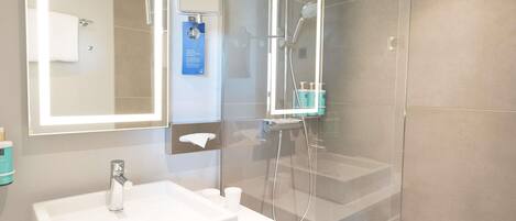 Un baño moderno con un espejo grande, un lavamanos y un box de ducha.