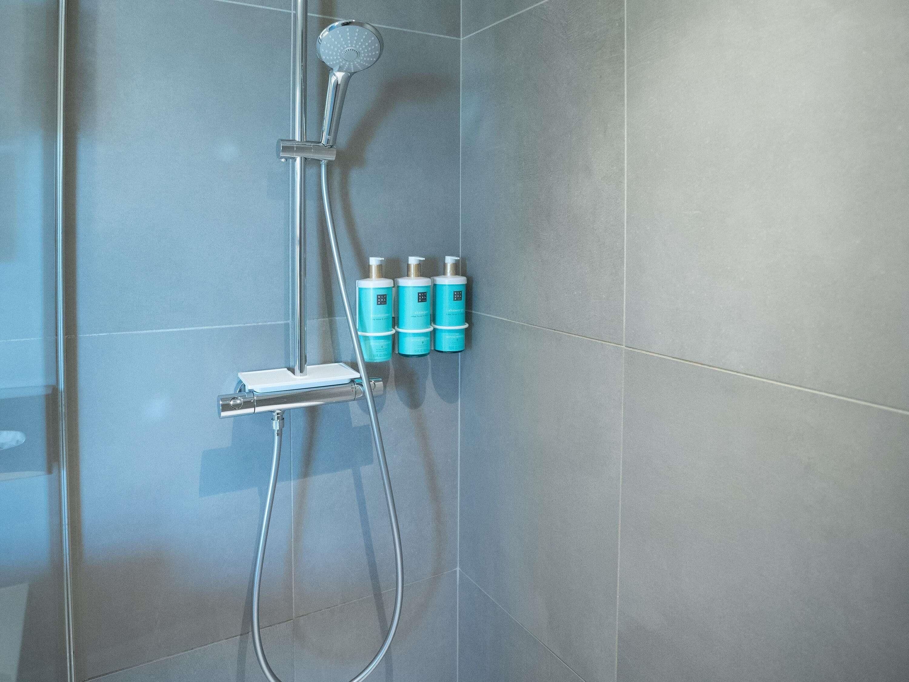 A shower with a handheld showerhead and three bottles of shampoo.