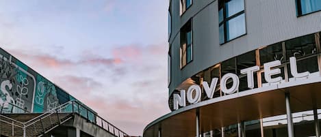 Un hotel llamado NOVOTEL con un diseño arquitectónico moderno, con ventanas grandes y una fachada curva.