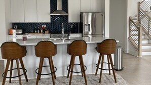 A modern kitchen with white cabinets, a stainless steel refrigerator, a herringbone backsplash, and a bar area with stools. - 5 Queen Bed 4 Full Bath Luxury Home, 1.4 miles to Bank of America Stadium (Charlotte)